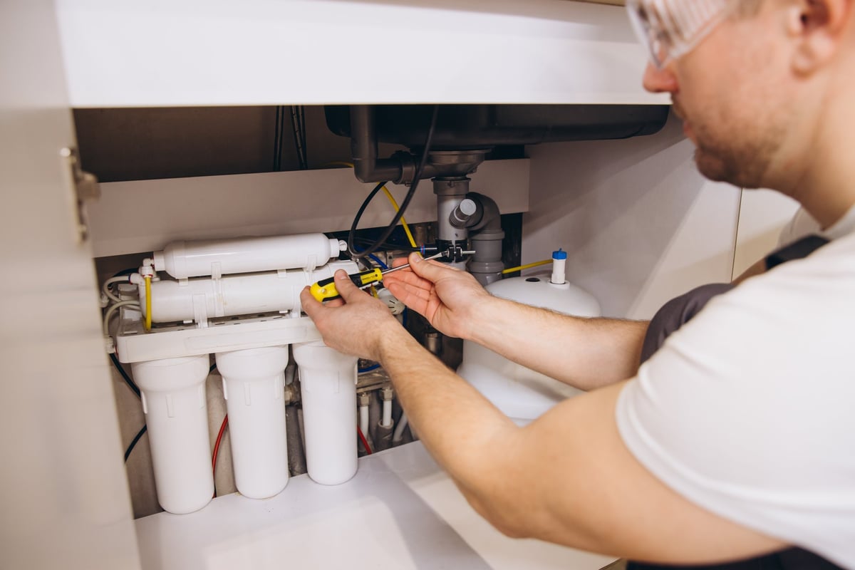 Loodgieter monteert waterfilter onder gootsteen